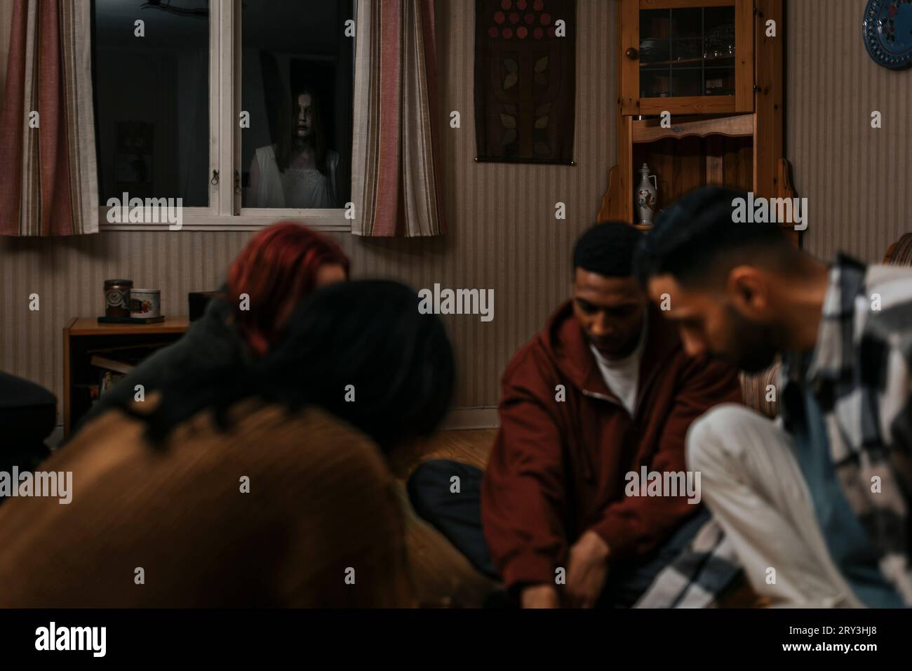 Ein Geist, der durch das Fenster auf Männer und Frauen im Spukhaus schaut Stockfoto
