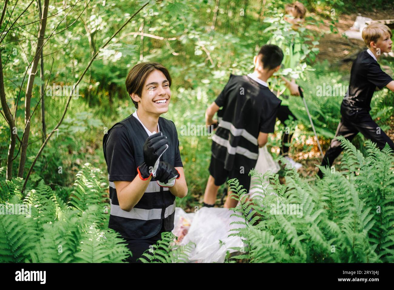 Fröhlicher Teenager mit Handschuhen, der inmitten grüner Pflanzen steht Stockfoto