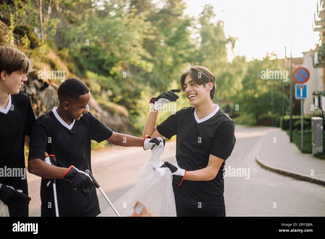 Fröhliche Teenager-Jungs mit Müllsäcken auf der Straße Stockfoto