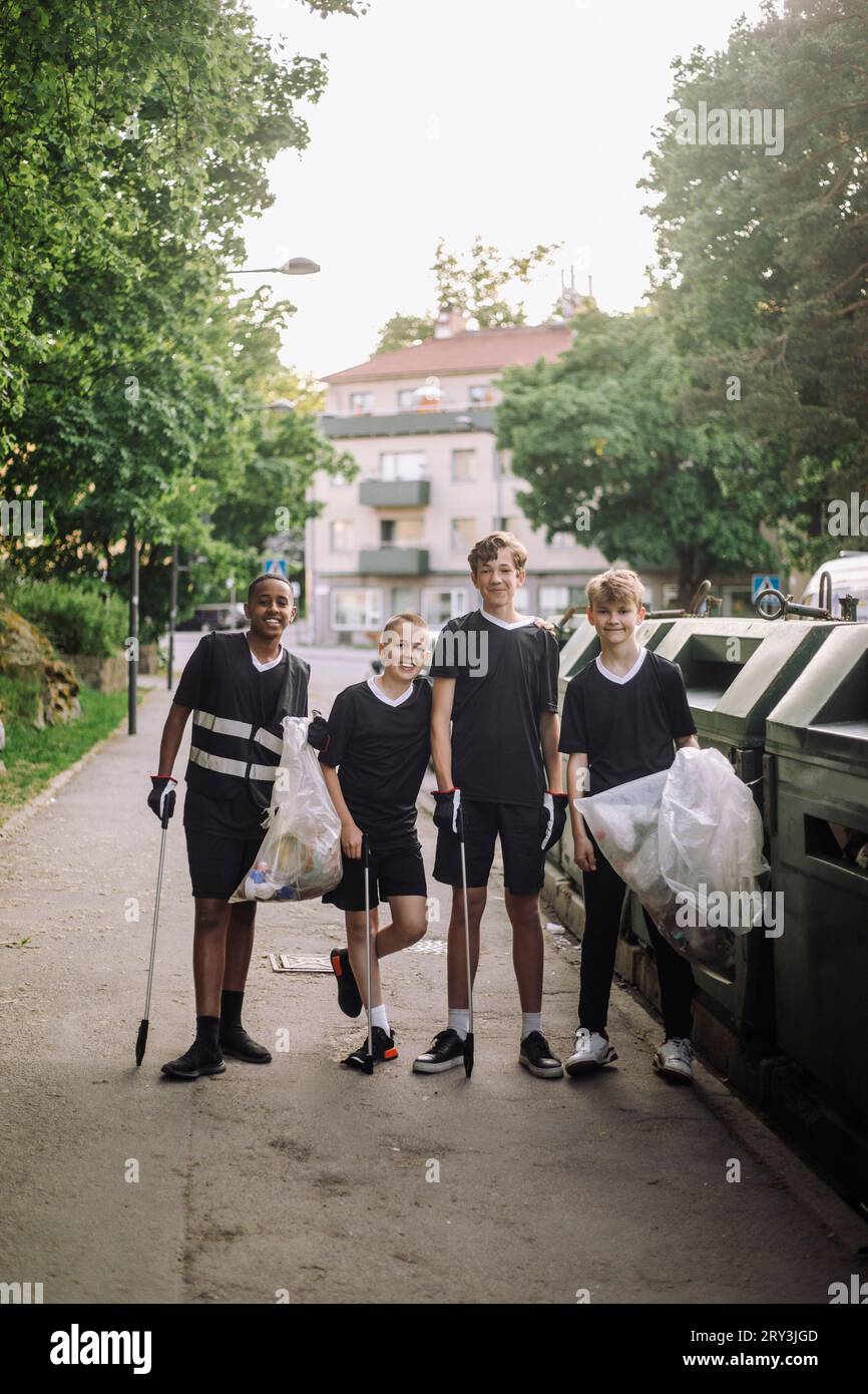 Porträt von lächelnden Jungen, die mit Müllsäcken stehen, indem sie Mülltonnen aufbereiten Stockfoto