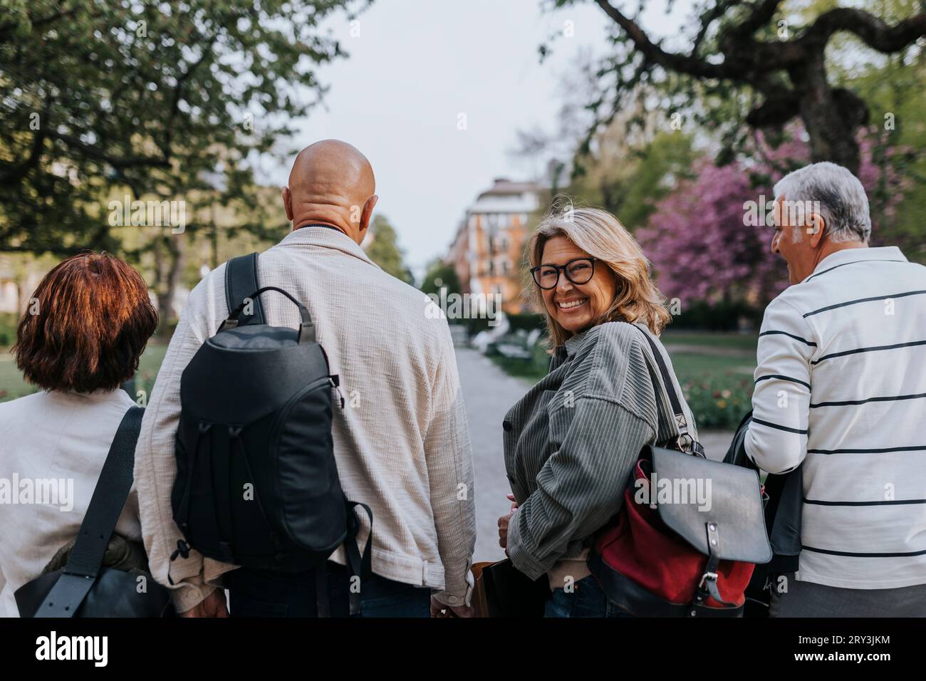 Porträt einer glücklichen Seniorin, die über die Schulter schaut, während sie mit Freunden im Park spaziert Stockfoto