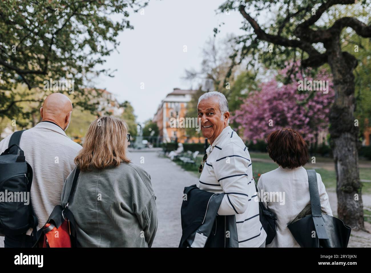 Porträt eines lächelnden älteren Mannes, der über die Schulter schaut, während er mit Freunden im Park spaziert Stockfoto