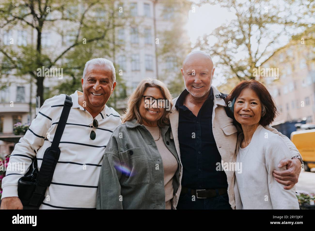 Porträt lächelnder älterer Freunde, die mit Armen auf der Straße stehen Stockfoto