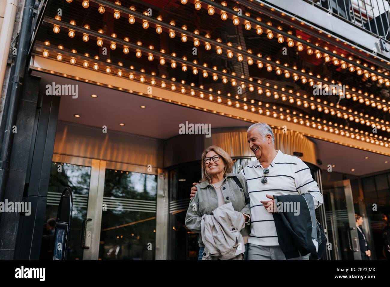 Glücklicher älterer Mann mit Arm um eine ältere Freundin, während er vor dem Kino steht Stockfoto