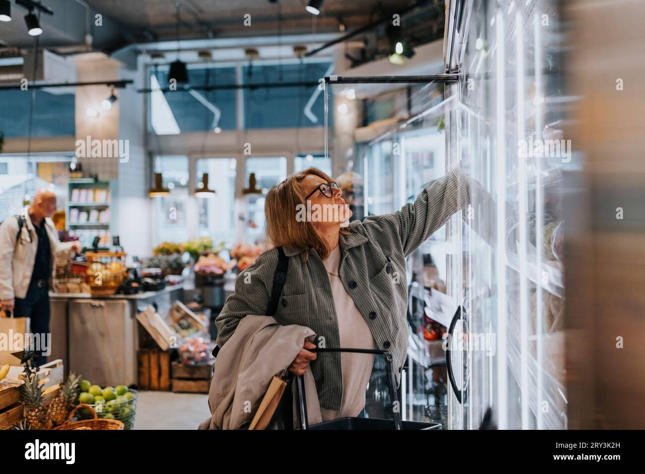 Eine ältere Frau, die nach Produkten greift, während sie im Supermarkt einkaufen Stockfoto