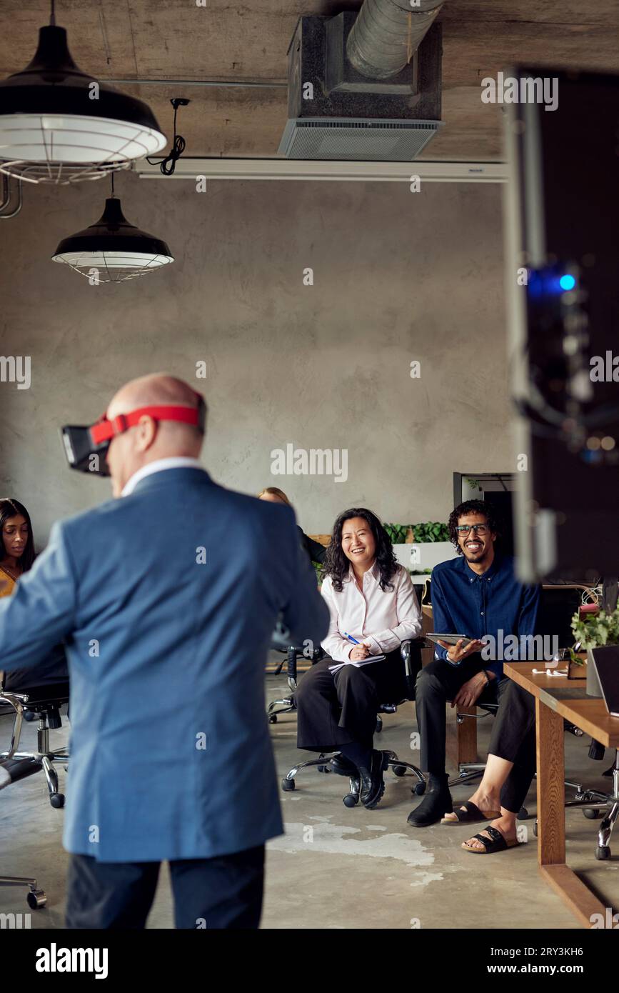 Lächelnde Kollegen, die einen reiferen Geschäftsmann mit VR im Büro sehen Stockfoto