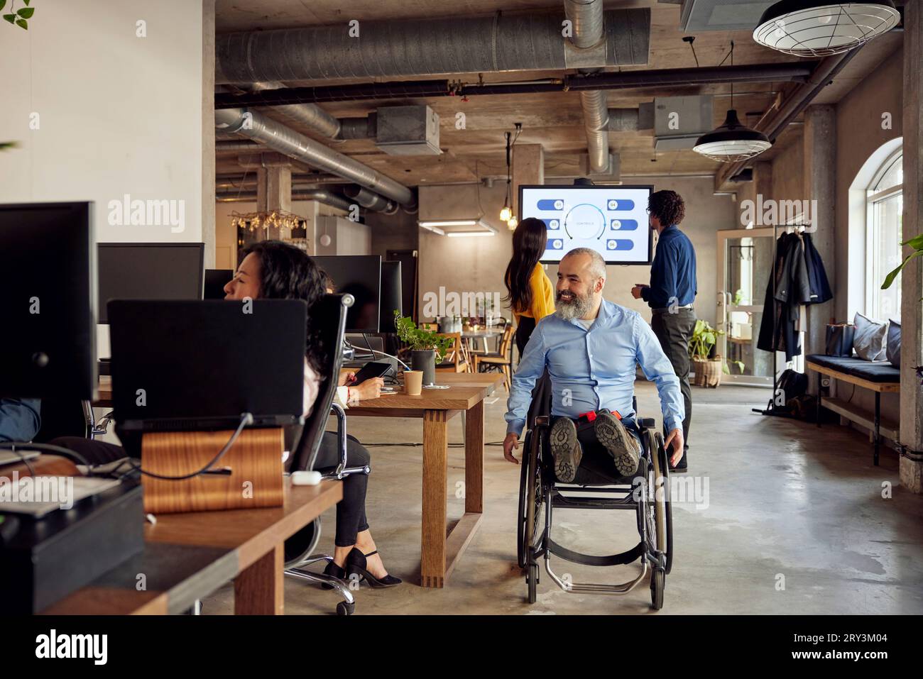Lächelnder Geschäftsmann mit Behinderung im Rollstuhl im Kreativbüro Stockfoto