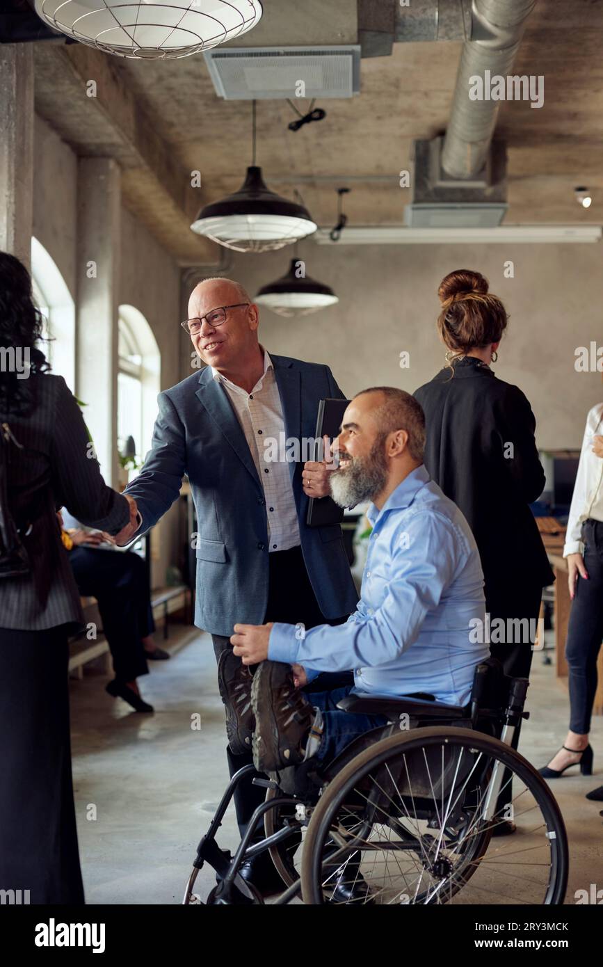 Geschäftsmann und Geschäftsfrau beim Handschlag eines männlichen Kollegen mit Behinderung im Büro Stockfoto