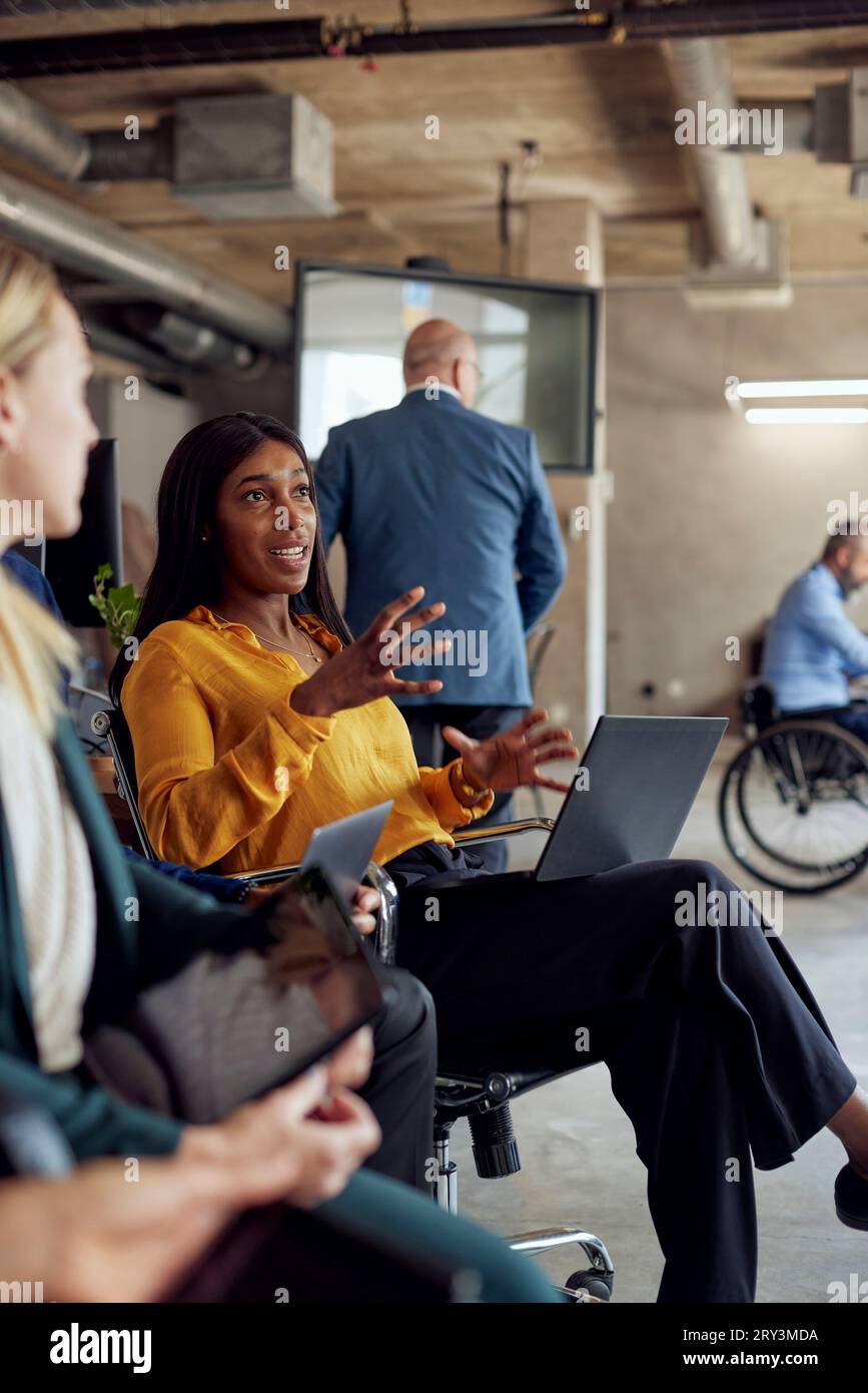 Selbstbewusste Geschäftsfrau mit Gesten, während sie im Büro von einer Kollegin sitzt Stockfoto