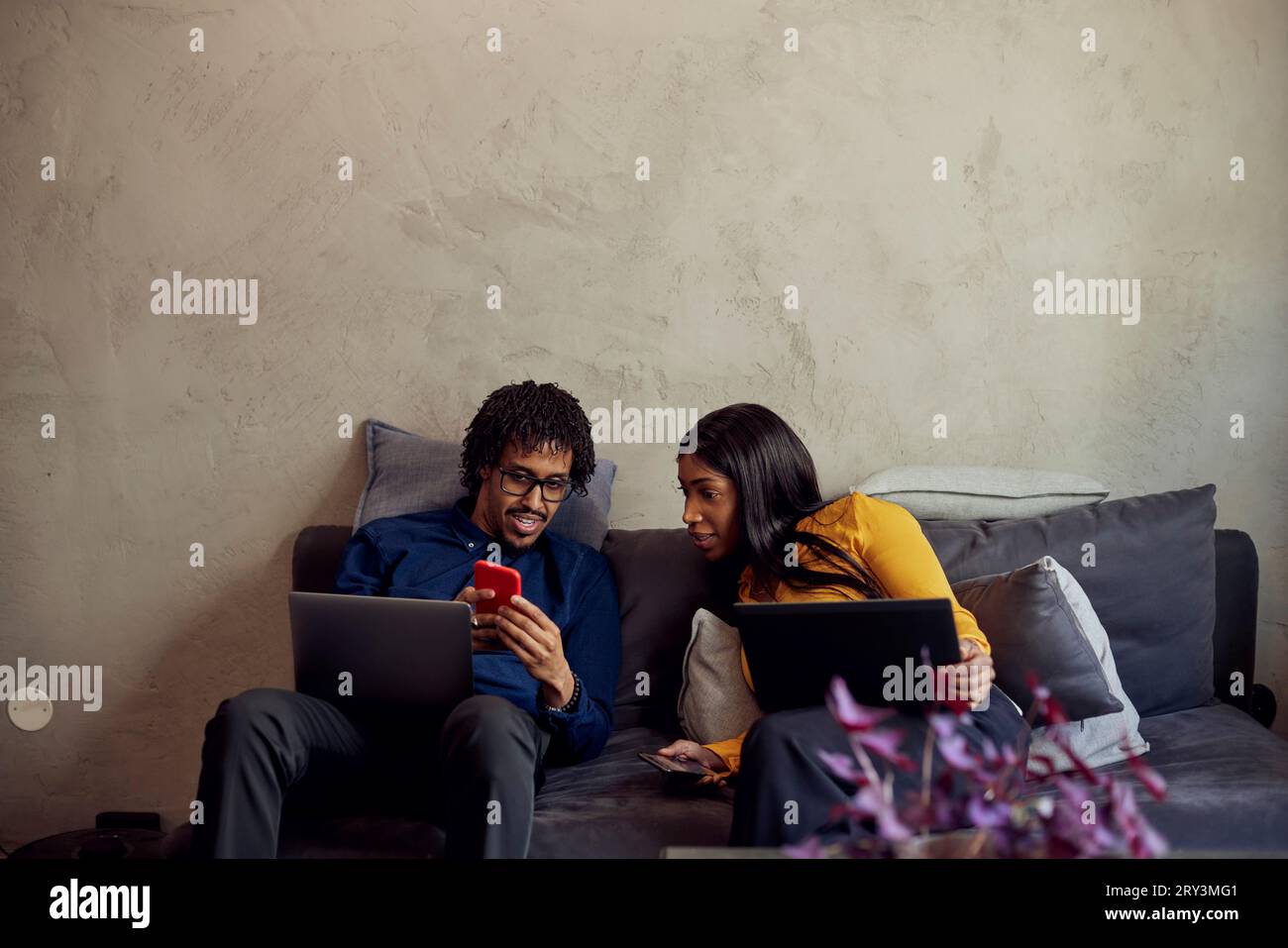 Geschäftsmann teilt sich das Smartphone mit Geschäftsfrau, die im Büro auf dem Sofa sitzt Stockfoto