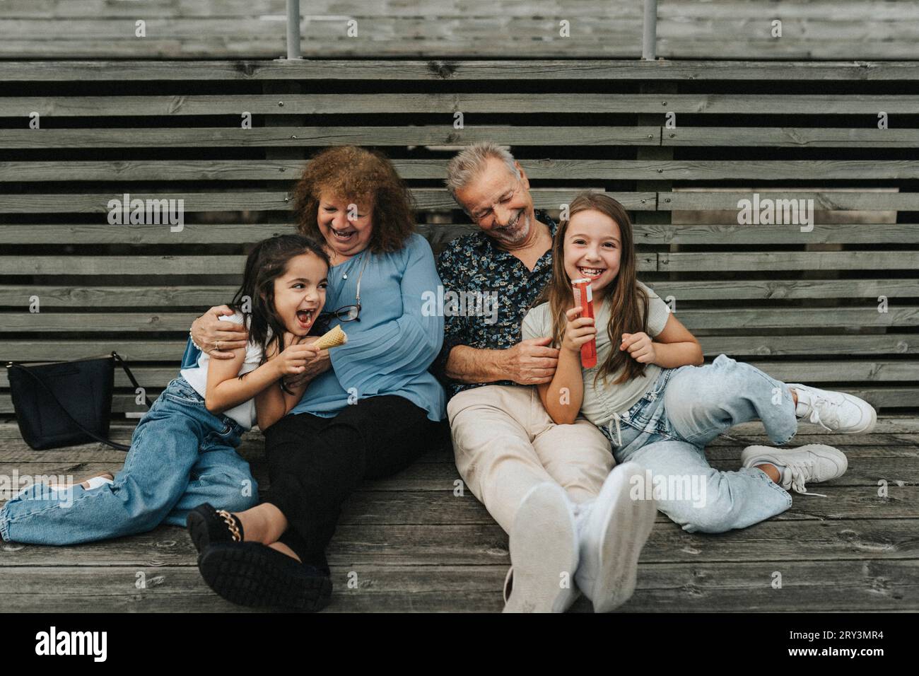 Die ganze Länge von glücklichen Großeltern und Enkelinnen, die auf Diele sitzen Stockfoto