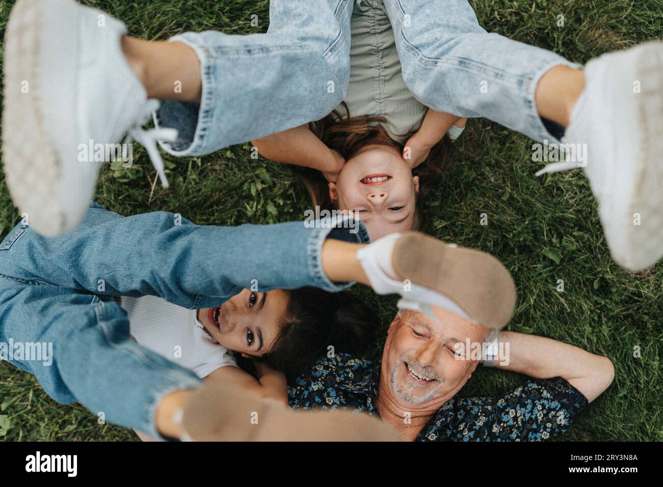Direkt über dem Blick auf einen älteren Mann mit Enkelinnen, die auf Gras liegen Stockfoto