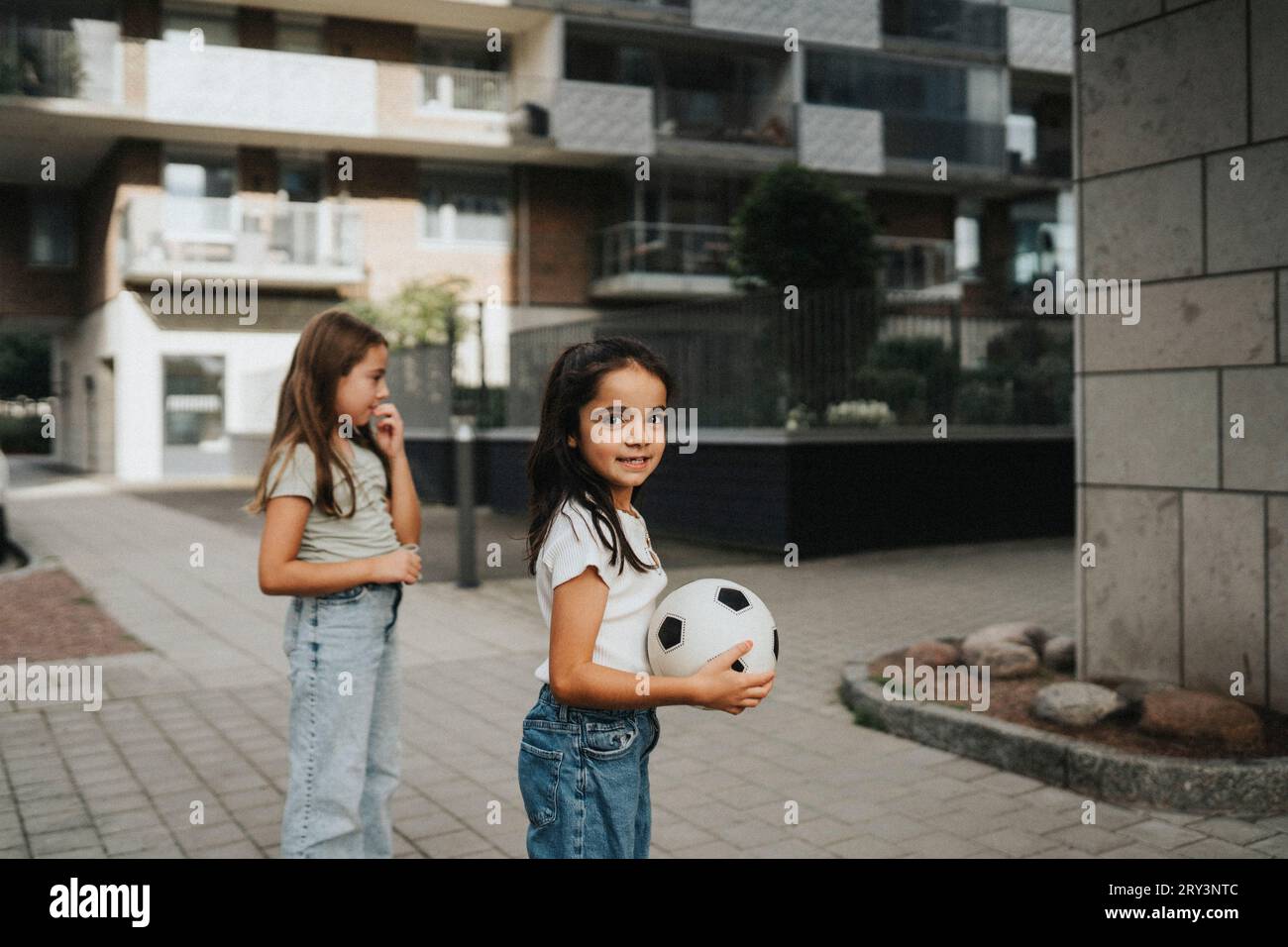 Mädchen, das Ball hält, während sie neben Schwester auf dem Fußweg steht Stockfoto