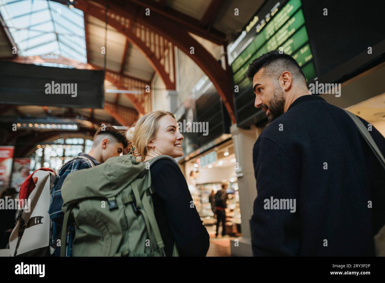 Lächelnde Frau, die Gepäck trägt, während sie mit einem Mann am Bahnhof redet Stockfoto