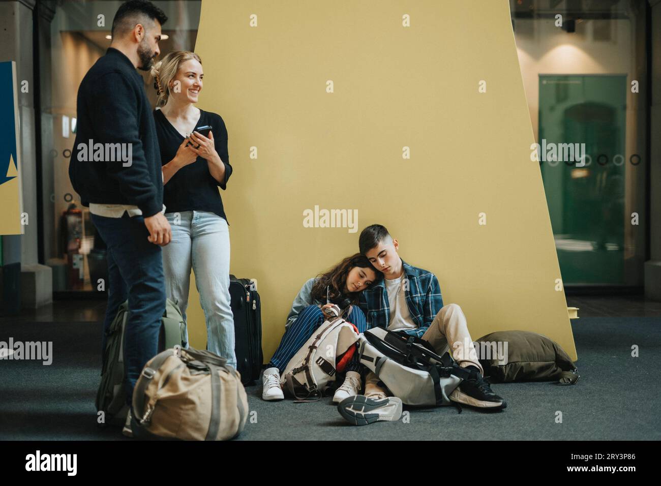 Mann und Frau stehen neben Kindern, die ein Nickerchen an der gelben Wand machen Stockfoto