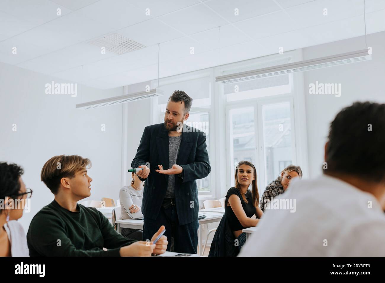 Professor unterrichten, während er mit männlichen Studenten im Klassenzimmer spricht Stockfoto
