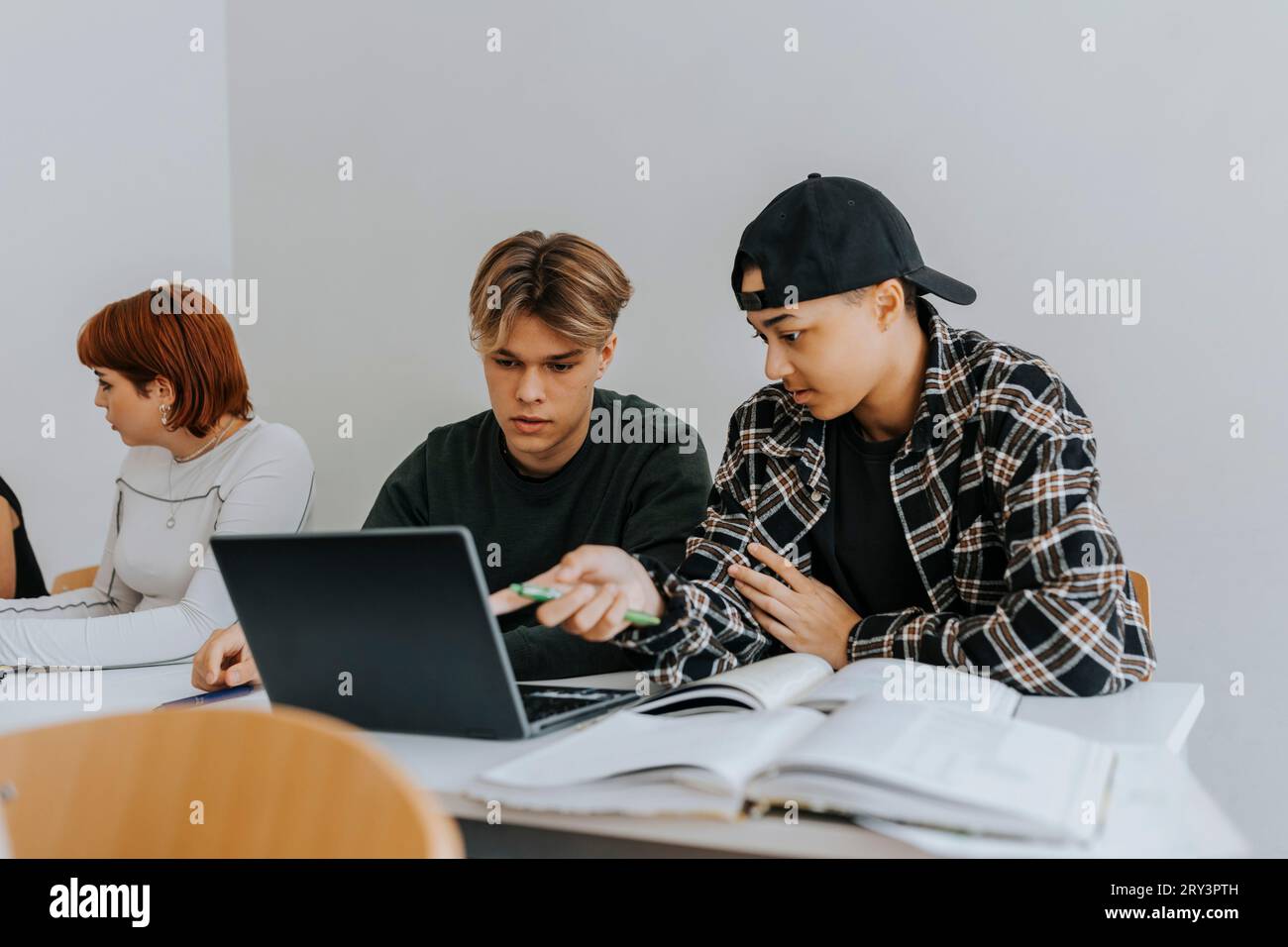 Männliche Schüler, die im Klassenzimmer am Schreibtisch mit dem Laptop zusammen arbeiten Stockfoto