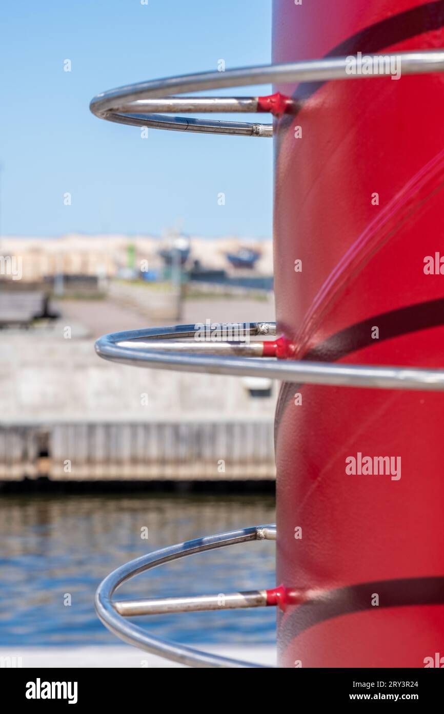 Industrie-, Metall-, große, burgunderfarbene Konstruktion mit geschwungenen glänzenden Rohren. Wasser, hölzerner Zaun, klarer Himmel und verschwommenes Ufer im Hintergrund. Copyspace Stockfoto