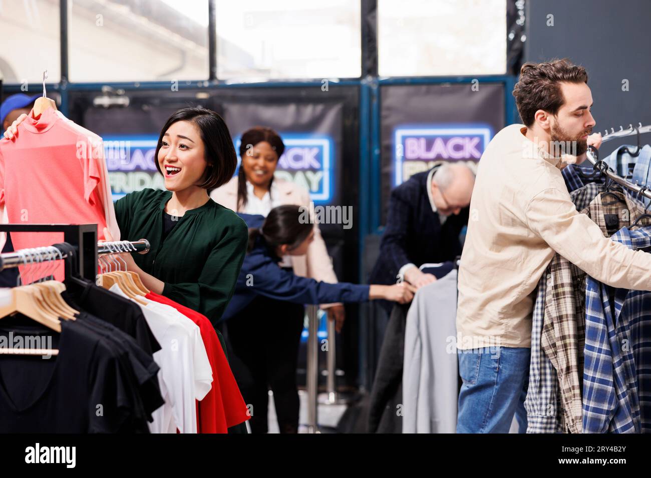 Saisonale Angebote im Bekleidungsgeschäft. Happy Excited Black Friday Shopper schnappen sich Kleidung zu ermäßigten Preisen und jagen nach Schnäppchen. Verschiedene Kunden, die gerne im Modegeschäft einkaufen Stockfoto