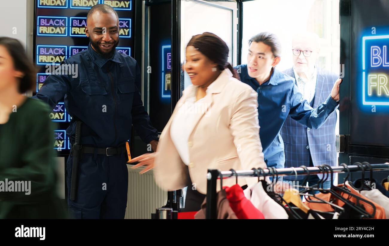 Wachtposten öffnen Türen bei Black friday Event und ermöglichen den Zugang zu Kleidung im Einkaufszentrum. Verschiedene Leute, die drinnen herumeilen, um Artikel zum halben Preis zu kaufen, finden die besten Rabatte auf die Räumung. Stockfoto