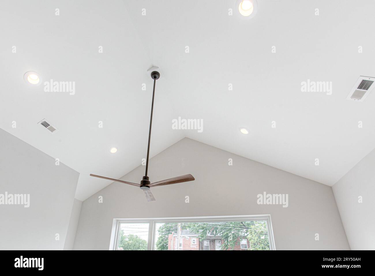 Stilvoller moderner Deckenventilator aus Holz und Schwarz mit gewölbter Decke und großen modernen Fenstern Stockfoto