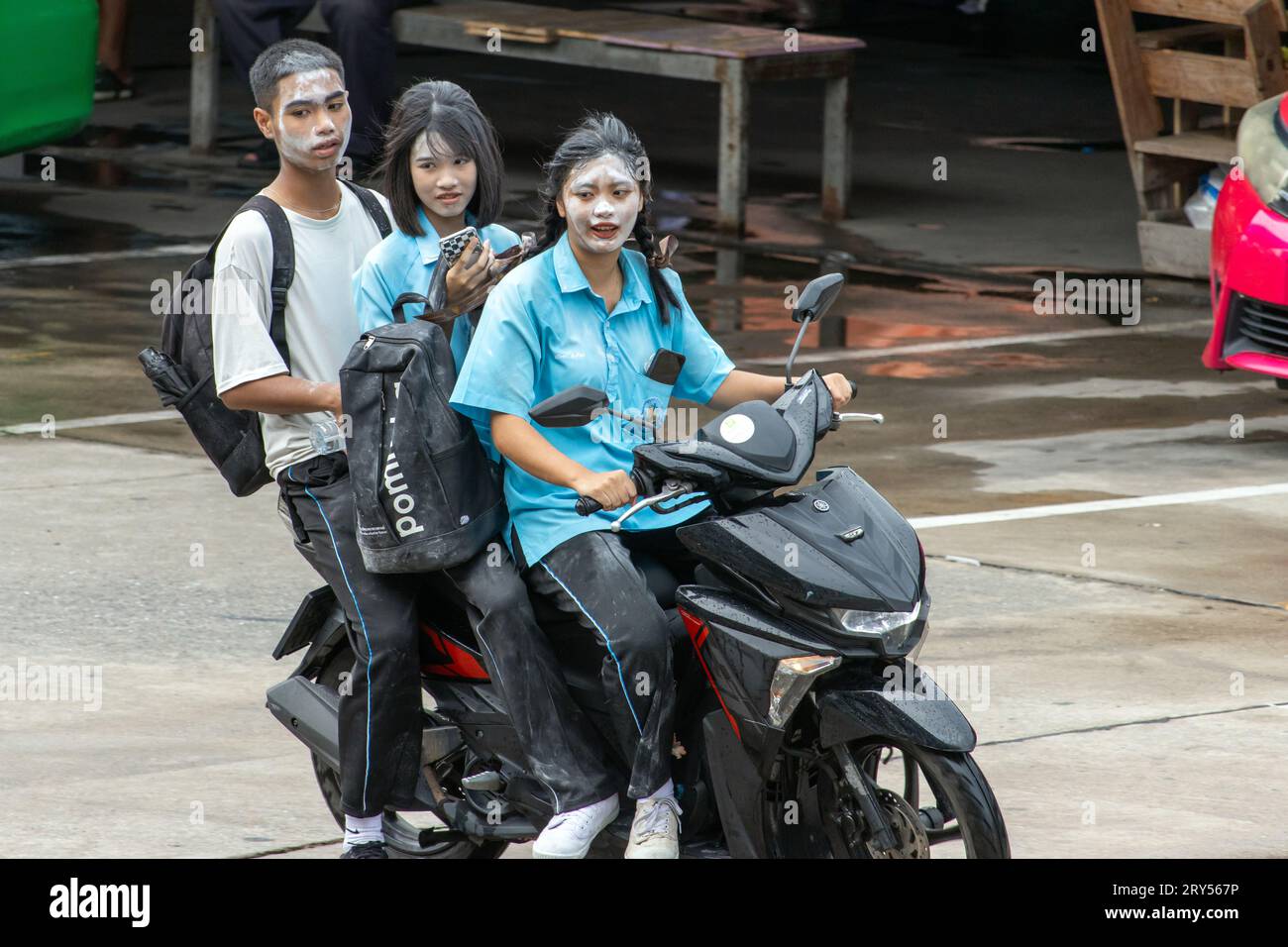 SAMUT PRAKAN, THAILAND, Juni 06 2023, Ein Trio von Teenagern mit Puder auf ihren Gesichtern, die mit einem Motorrad im Regen fahren Stockfoto