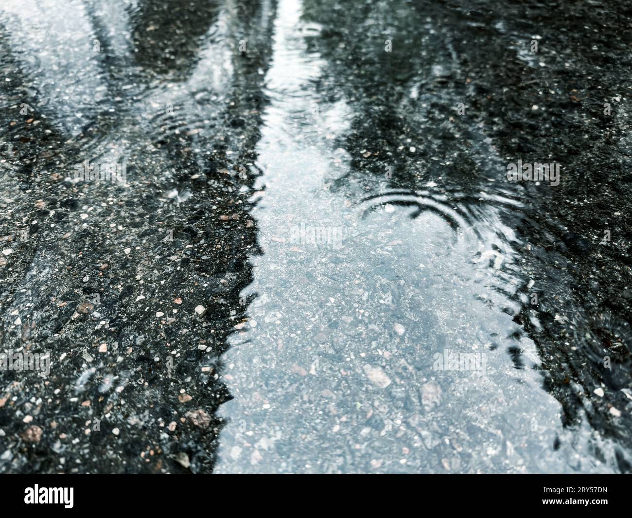 Überfluteter Straßenbelag nach starkem Regen. Wasserpfütze mit Regentropfen und Spiegelungen des Himmels. Stockfoto