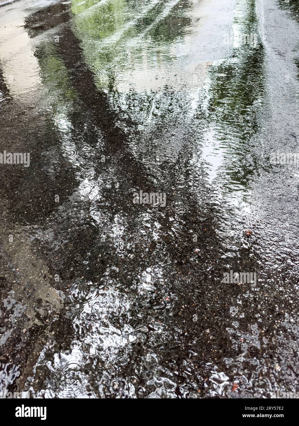 Wasserpfützen auf Asphaltstraße mit einem Spiegelbild des bewölkten Himmels. Regen in der Stadt. Stockfoto