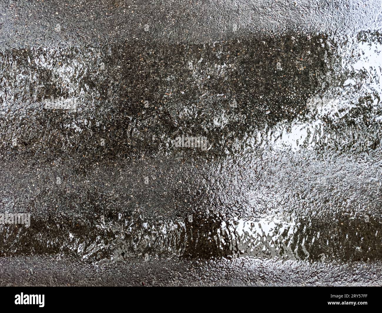 Nasse, dunkle Asphaltstraße nach starkem Regen. Himmelsreflexionen in der nassen Oberfläche. Stockfoto