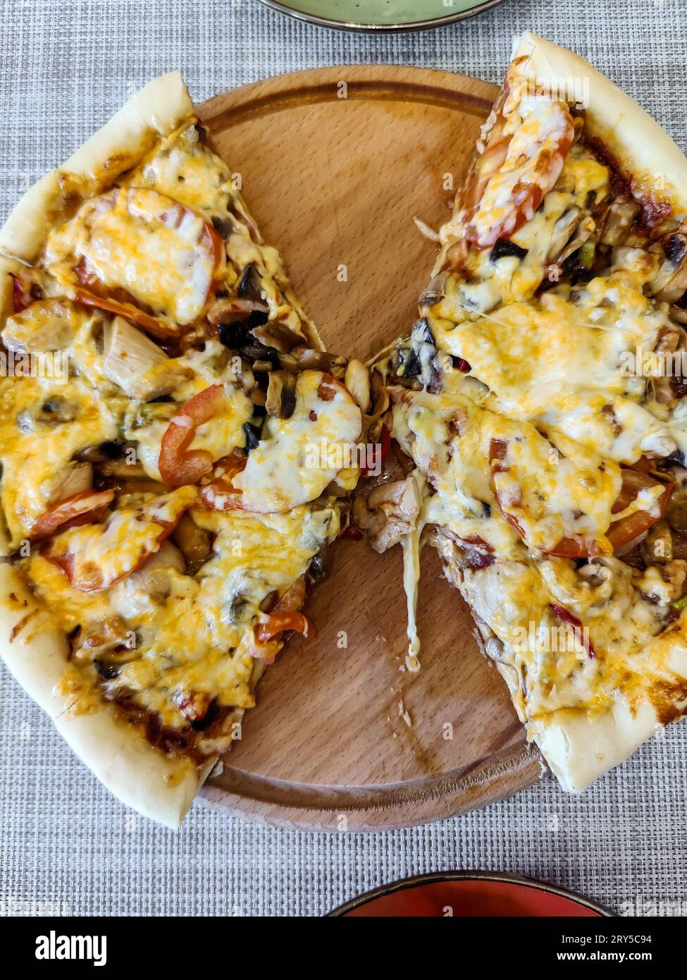 Köstliche hausgemachte Pizza in Scheiben mit Tomaten, Oliven, Hähnchenfleisch, Pilzen und gefüllt mit Käse. Übriggebliebene Pizza auf einem Holzteller. Draufsicht. Sel Stockfoto