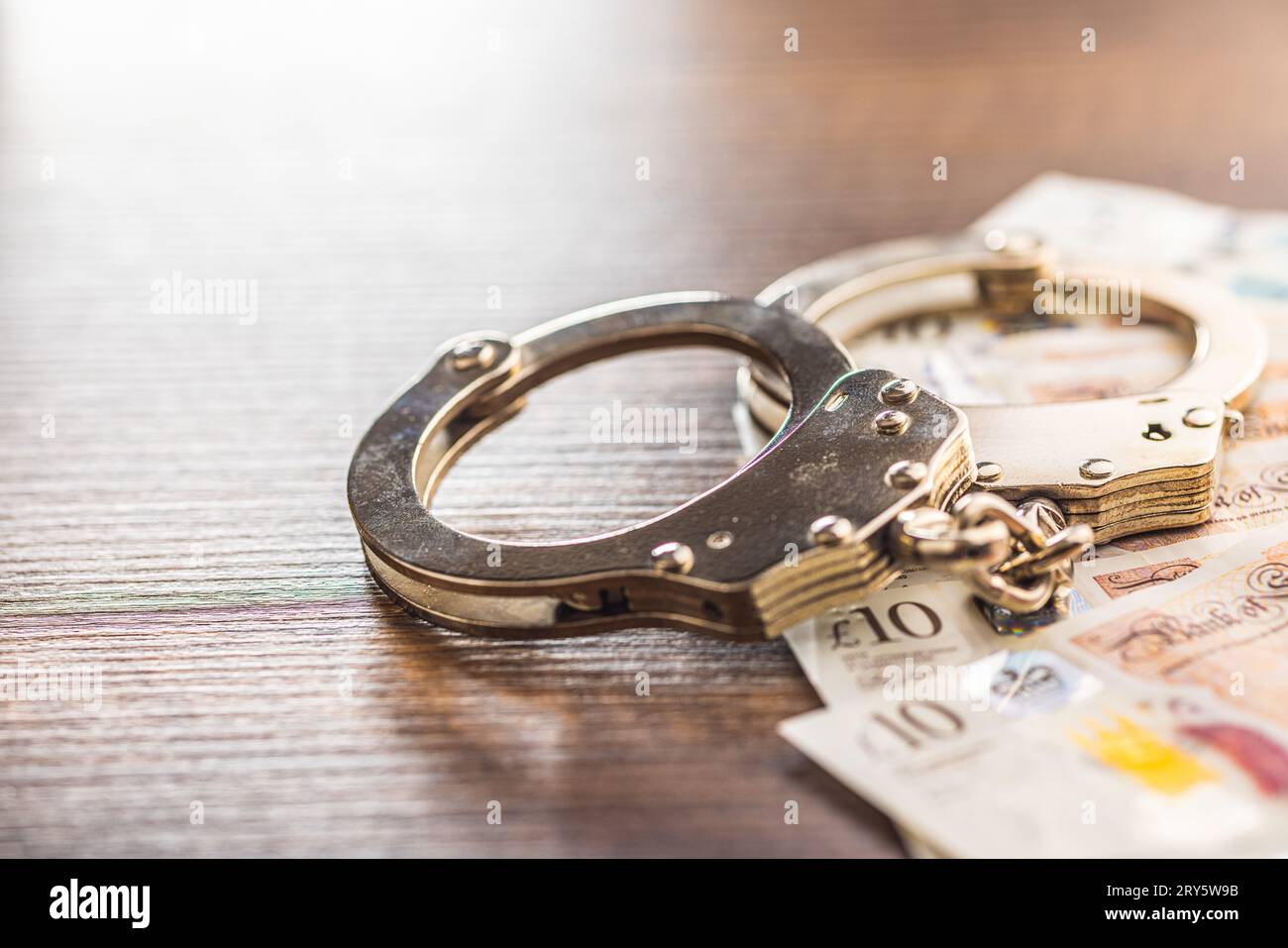 Handschellen und britisches Pfund Sterling auf dem Holztisch. Stockfoto