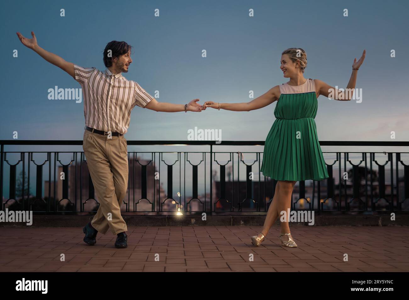 Die beiden schwingen auf einer Terrasse und tanzen im Profil, während sie die Hände halten. Die weitläufige Kulisse bietet viel Platz für Text. Stockfoto