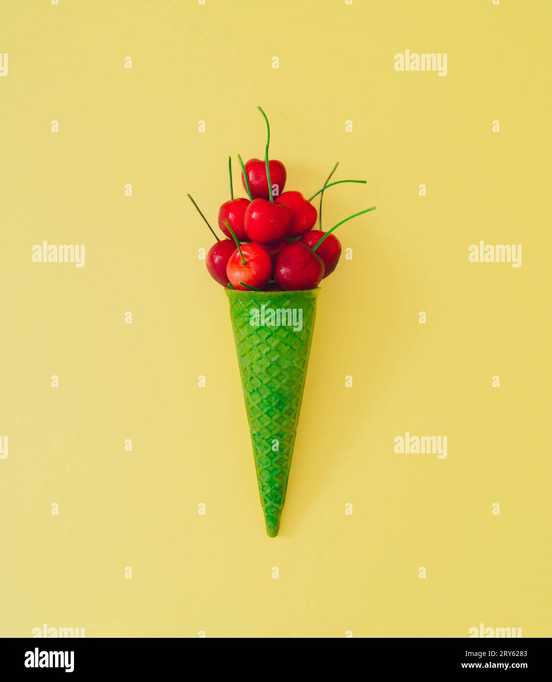Rote Kirschfrucht in grünem Kegel auf pastellgelbem Hintergrund. Minimales Sommerfrucht-Konzept. Kreative Sommereis-Idee. Flache Kirschanordnung. Stockfoto