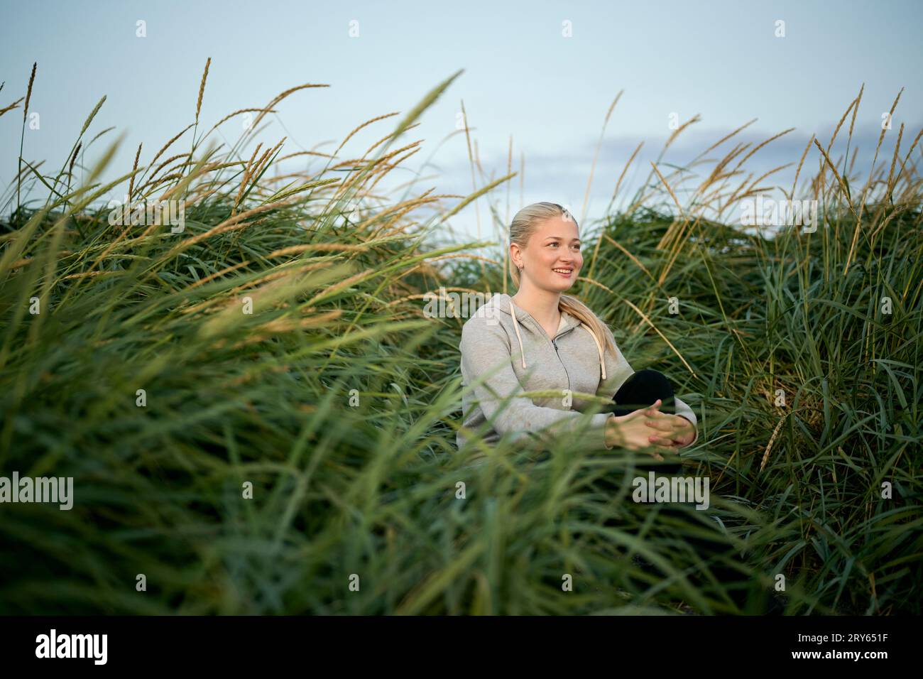 Lächelnde Frau, die auf dem Feld sitzt und das Knie umschließt Stockfoto