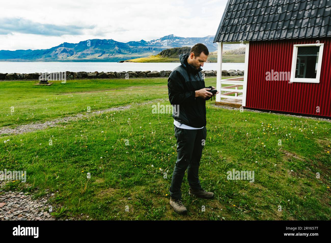 Der Mann fliegt Drohne an der roten Hütte über Fjorde und mit Bergen Stockfoto