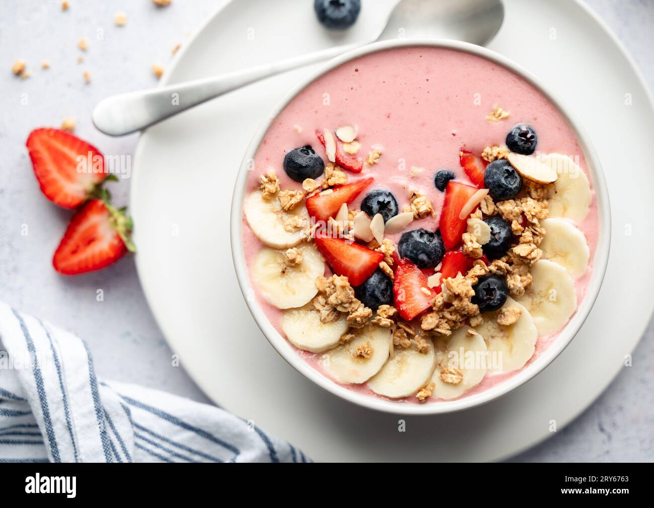 Blick von oben auf die Smoothie-Schüssel mit Obst und Müsli auf grauem Hintergrund. Stockfoto