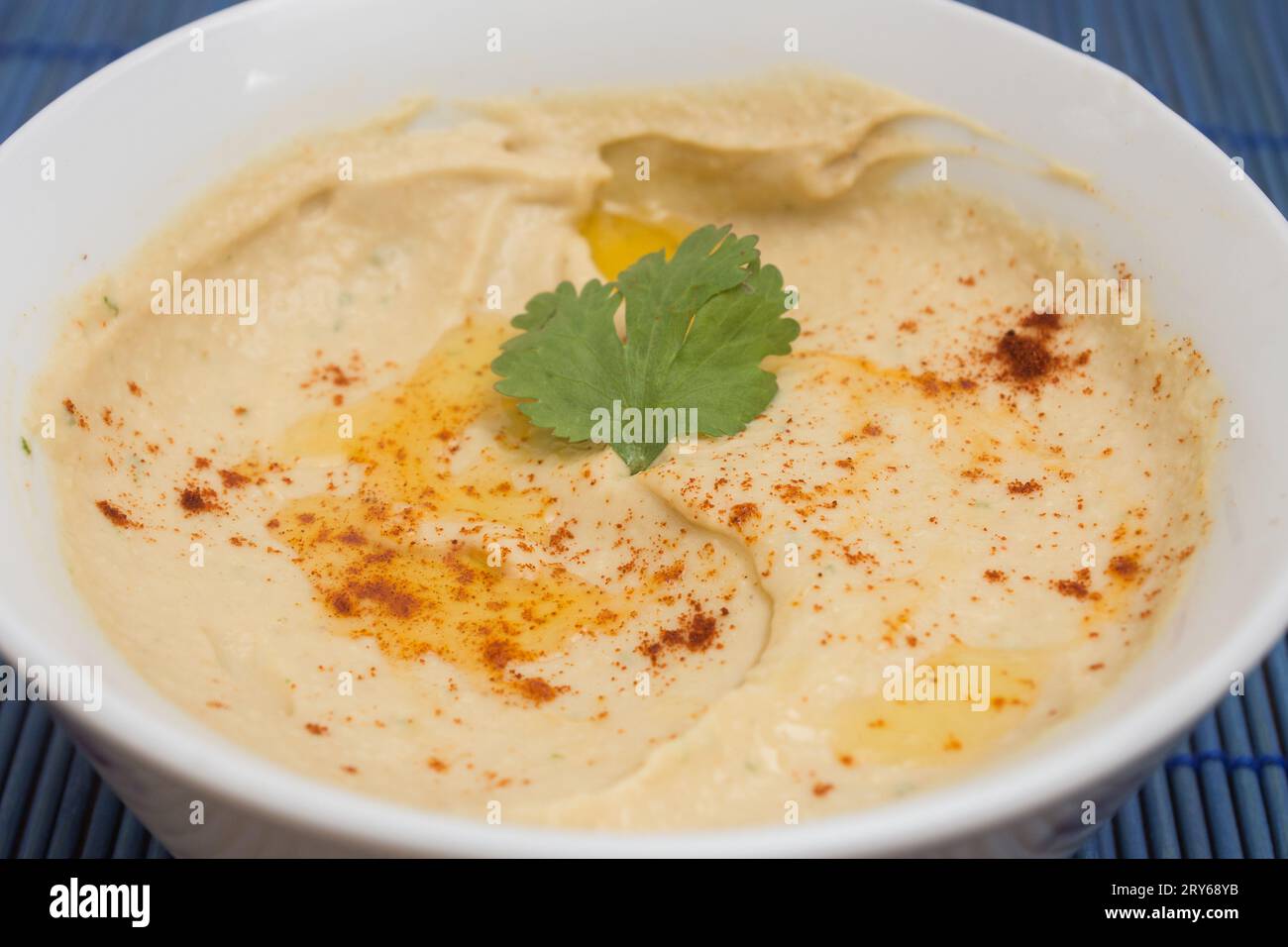Nahaufnahme von hausgemachtem Kichererbsen-Hummus, geschmückt mit einem Blatt frischen Koriander, Paprika und Olivenöl. Overhead View mit lebendigen Farben und Irresi Stockfoto