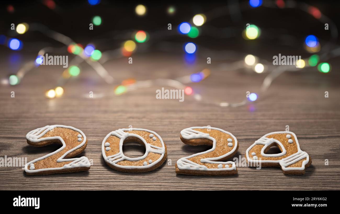 Nahaufnahme von Lebkuchenziffern auf Holz und farbiger LED-Lichtschnur im unscharfen Hintergrund mit Bokeh. Golden Baked Sweets for Happiness im Neujahrsfest 2024. Stockfoto