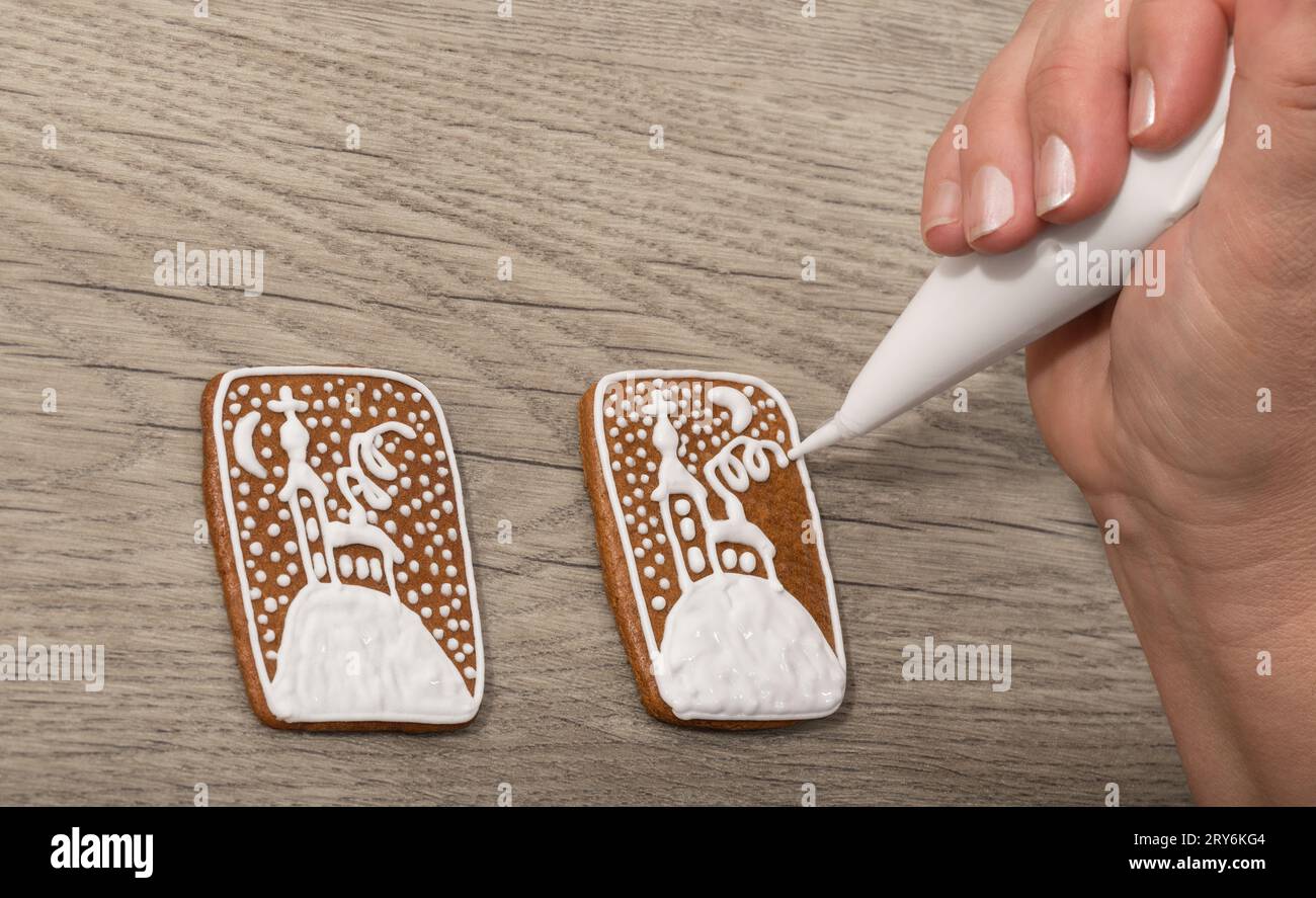 Nahaufnahme der Dekoration von WeihnachtsLebkuchen durch Paspelbeutel auf hölzernem Hintergrund. Weibliche Handmalerei Winterkirche auf süßen gebackenen Keksen. Weihnachtsgebäck. Stockfoto