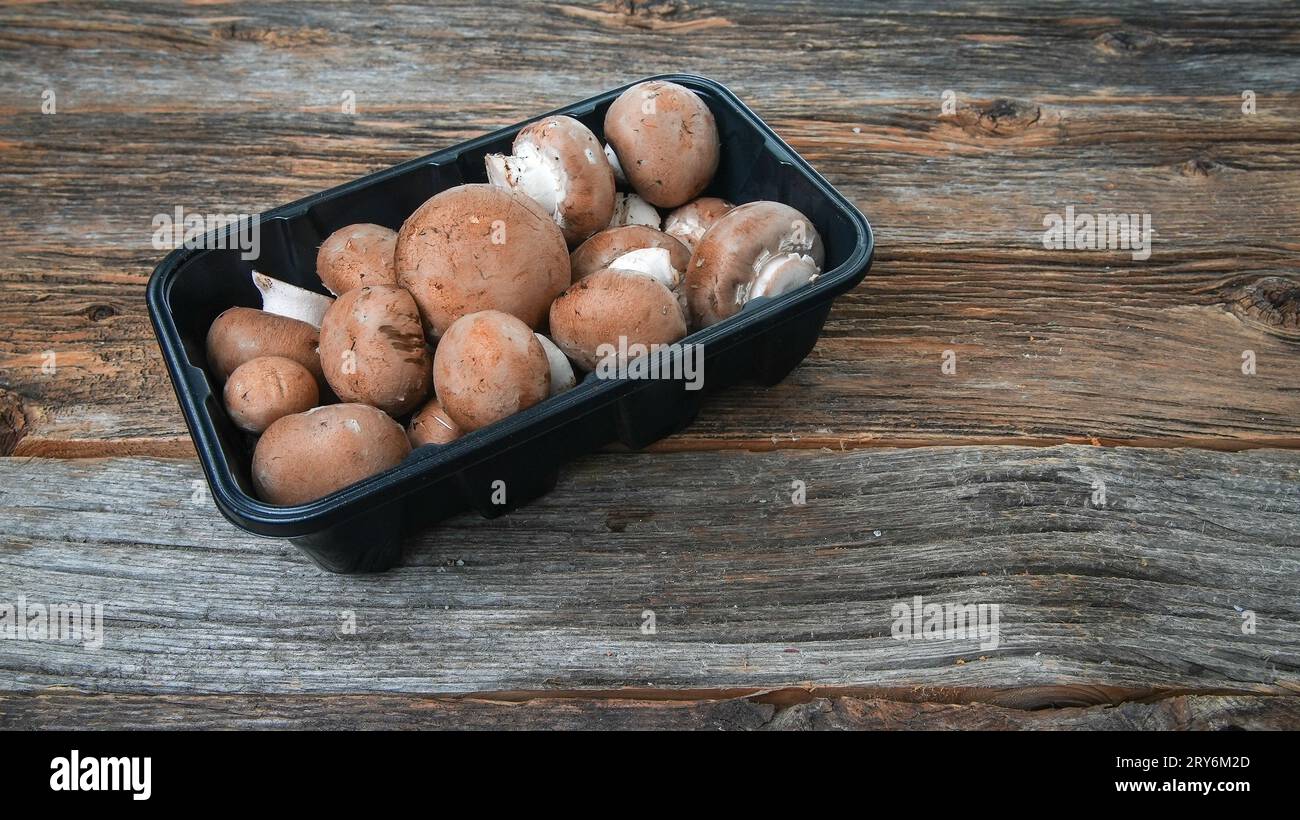 Baby-Bella-Pilze in Plastikverpackung auf rustikalem Tisch Stockfoto