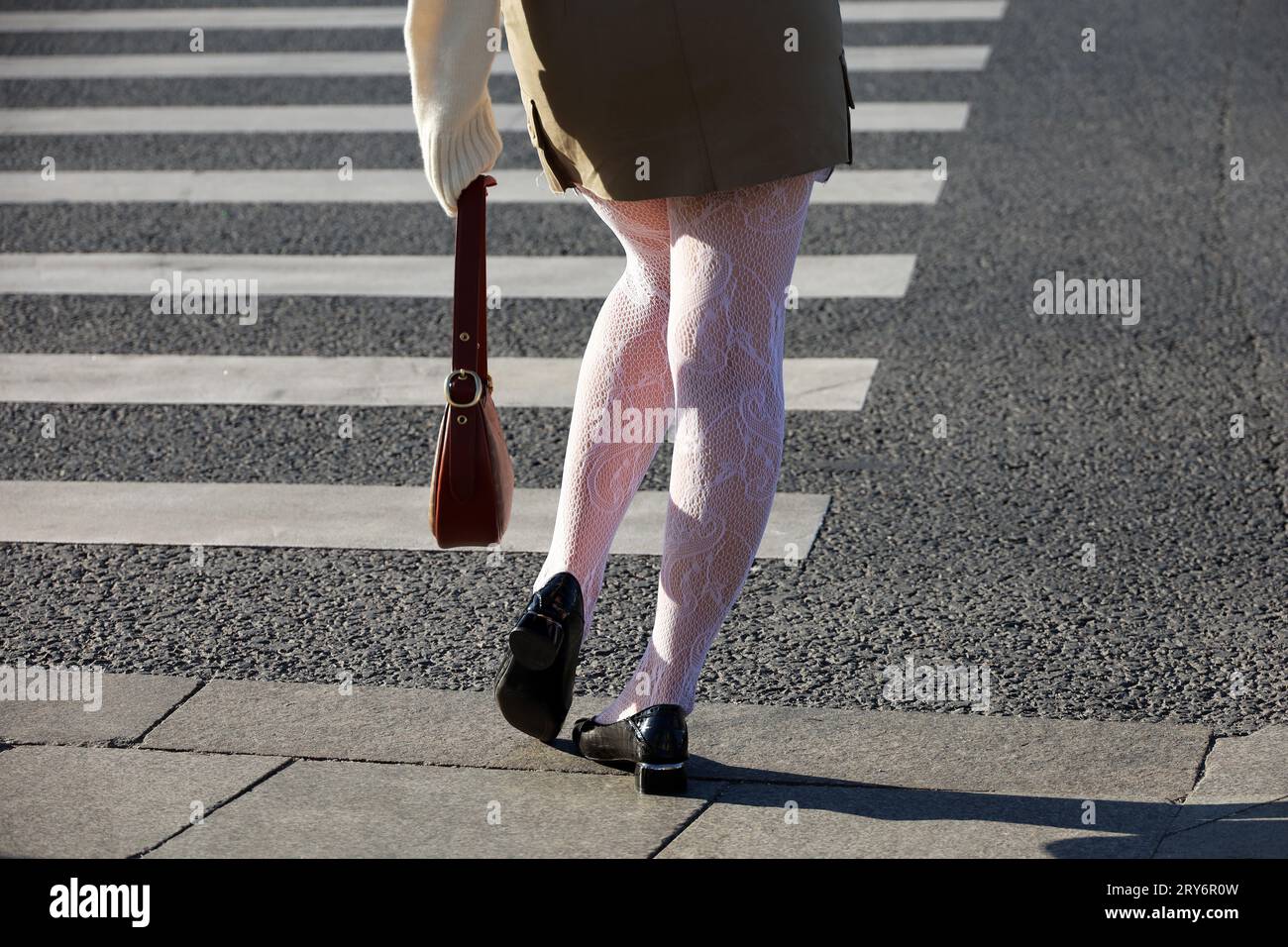 Weibliche Beine in weißen Strumpfhosen und schwarzen Schuhen auf Fußgängerübergängen. Schlankes Mädchen auf einer Straße mit Handtasche in der Hand, Mode in Herbststadt Stockfoto