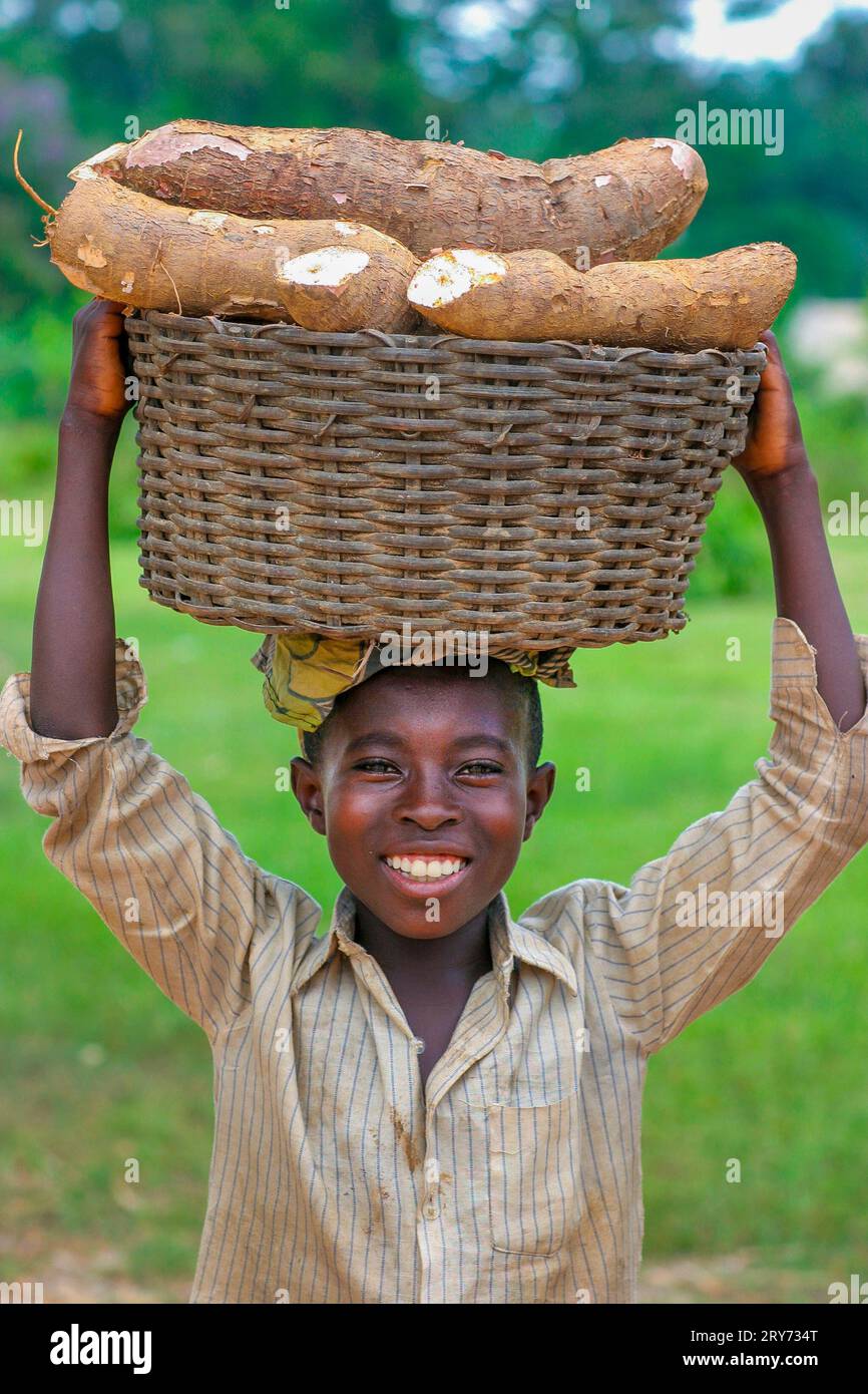 Ghana, Region Accra. Junge mit Kassavenernte. Die Wurzeln in einem Korb auf dem Kopf tragen. Stockfoto