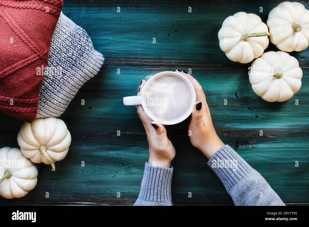 Die Hände der Frau halten heiße, dampfende Tasse Kaffee über einem rustikalen grünen Tisch mit Herbstpullover und weißen Kürbissen. Ansicht der Tischaufsicht. Stockfoto