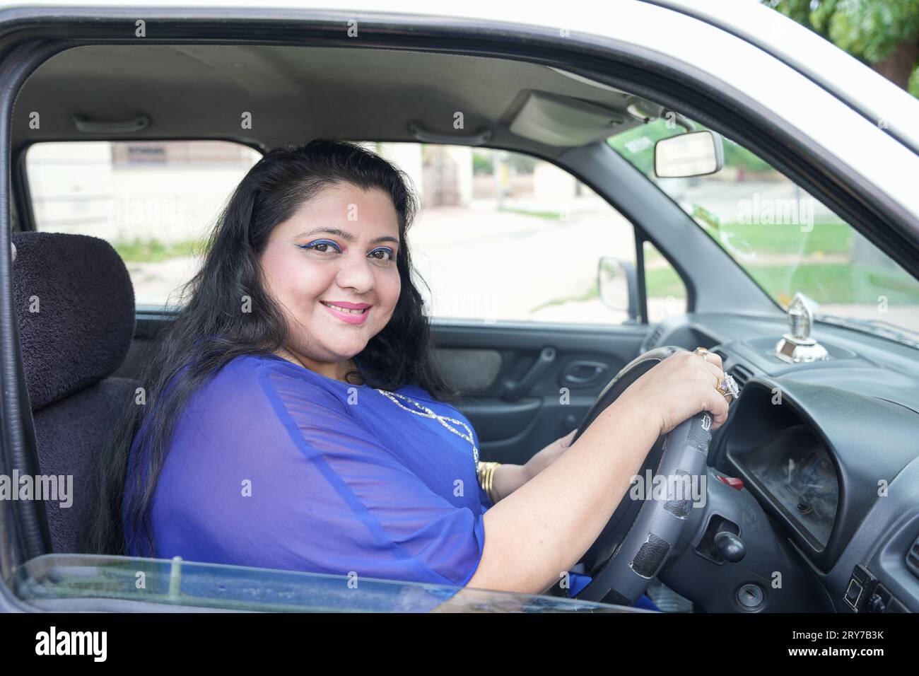 Glückliche indianerin in Übergröße, die im Auto sitzt, ohne den Sicherheitsgurt zu tragen und mit einem Lächeln auf die Kamera zu blicken. Stockfoto