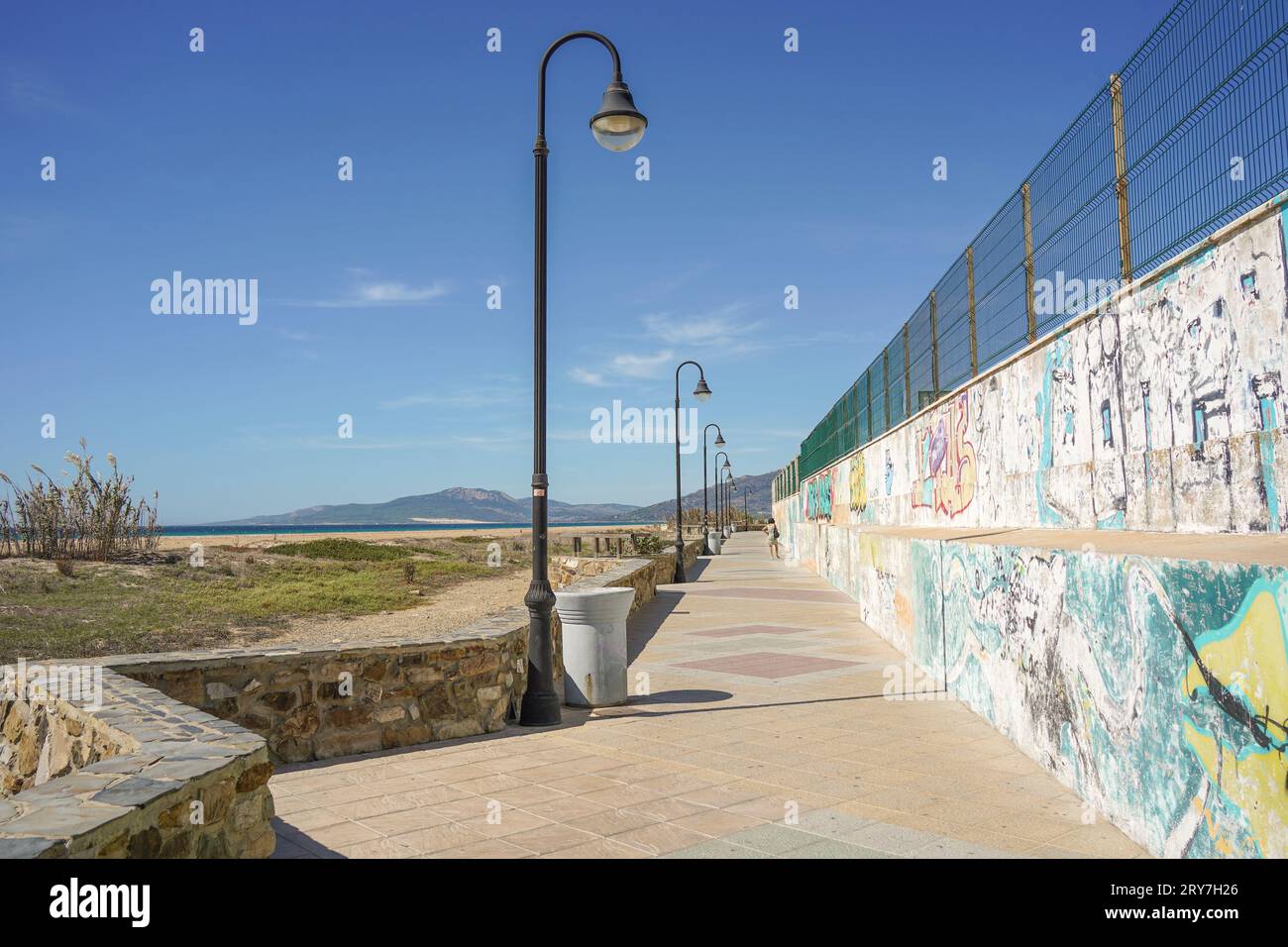 Fußgängerweg, Promenade mit Straßenlaternen und Graffiti an der Wand neben dem Strand, Tarifa, Spanien. Stockfoto
