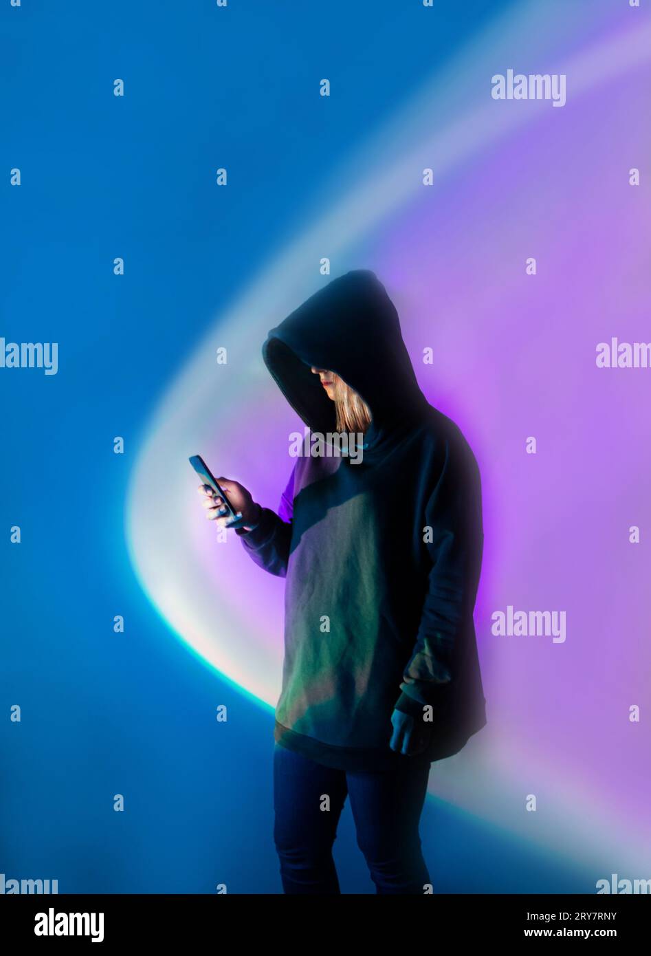 Schutz personenbezogener Daten auf einem Mobilgerät. Anonymer Mensch mit Mobiltelefon gegen helles, mehrfarbiges Neonlicht. Stockfoto