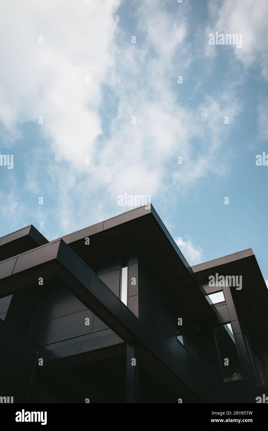 Blick auf ein modernes luxuriöses Architekturhaus mit schwarzen Oberflächen und einem modernen Design mit scharfem Winkel vor einem blauen Himmel mit Wolken Stockfoto
