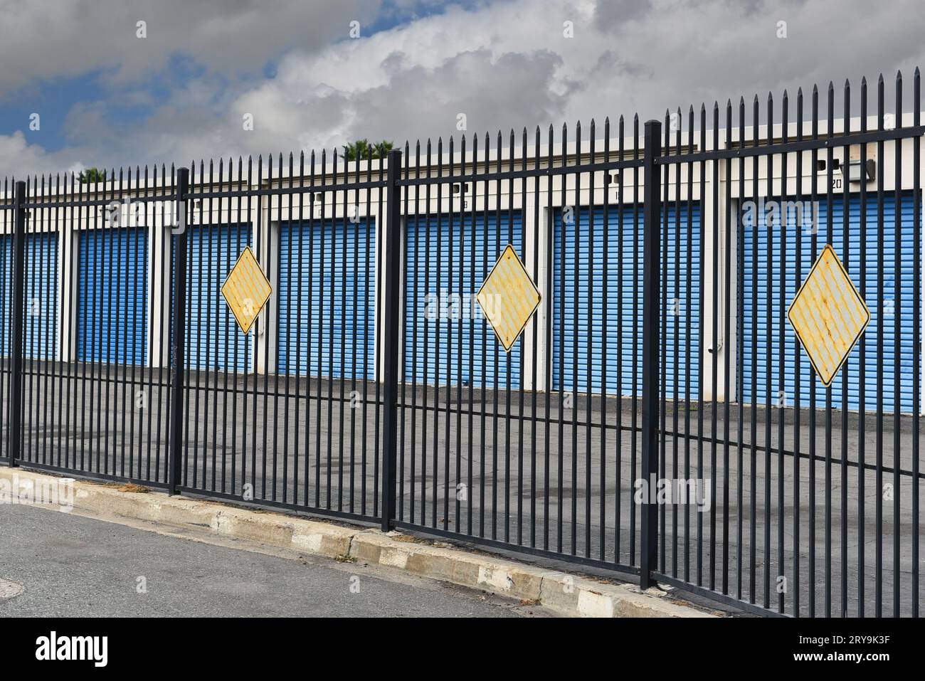 STANTON, KALIFORNIEN - 17. SEPTEMBER 2023: Ein schwarzer schmiedeeiserner Zaun, der eine Lagereinrichtung mit einer Reihe geschlossener blauer Türen umgibt. Stockfoto