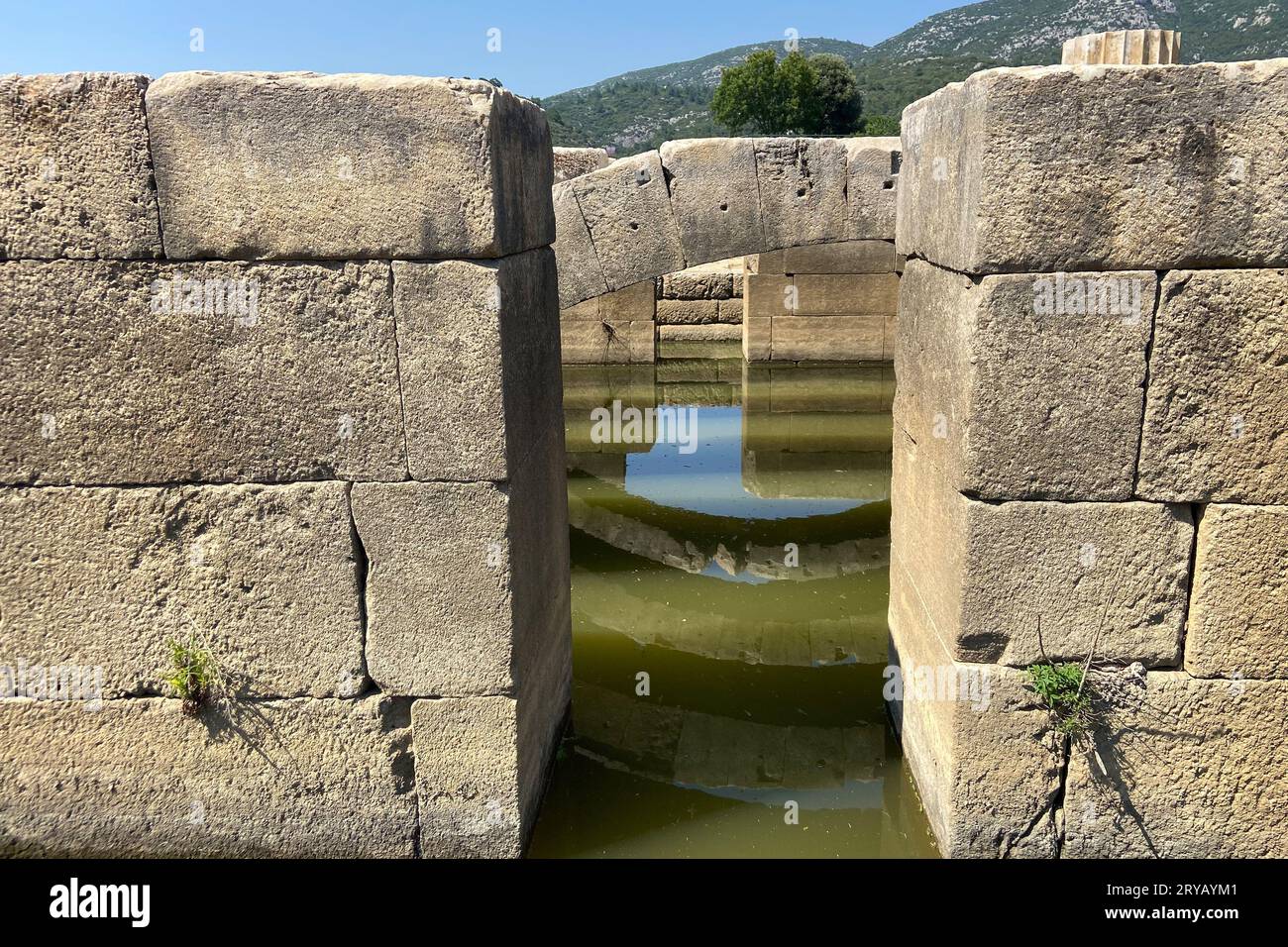 Deckenruinen des antiken Steintempels des Apollon in der antiken Stadt Klaros füllten Wasser, obere Bögen und Schlüsselsteine mit Reflexionen unter blauem Himmel İzmir Stockfoto