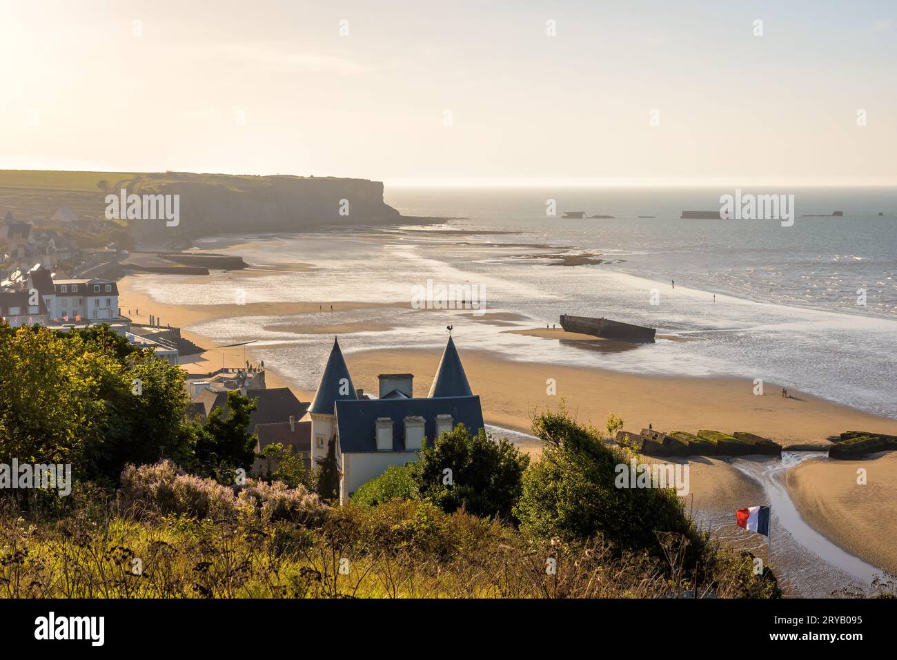 Blick auf den Strand von Arromanches in der Normandie bei Sonnenuntergang mit Überresten des Mulberry Hafens aus dem Zweiten Weltkrieg auf dem Sand und den Phoenix Caissons im Meer. Stockfoto